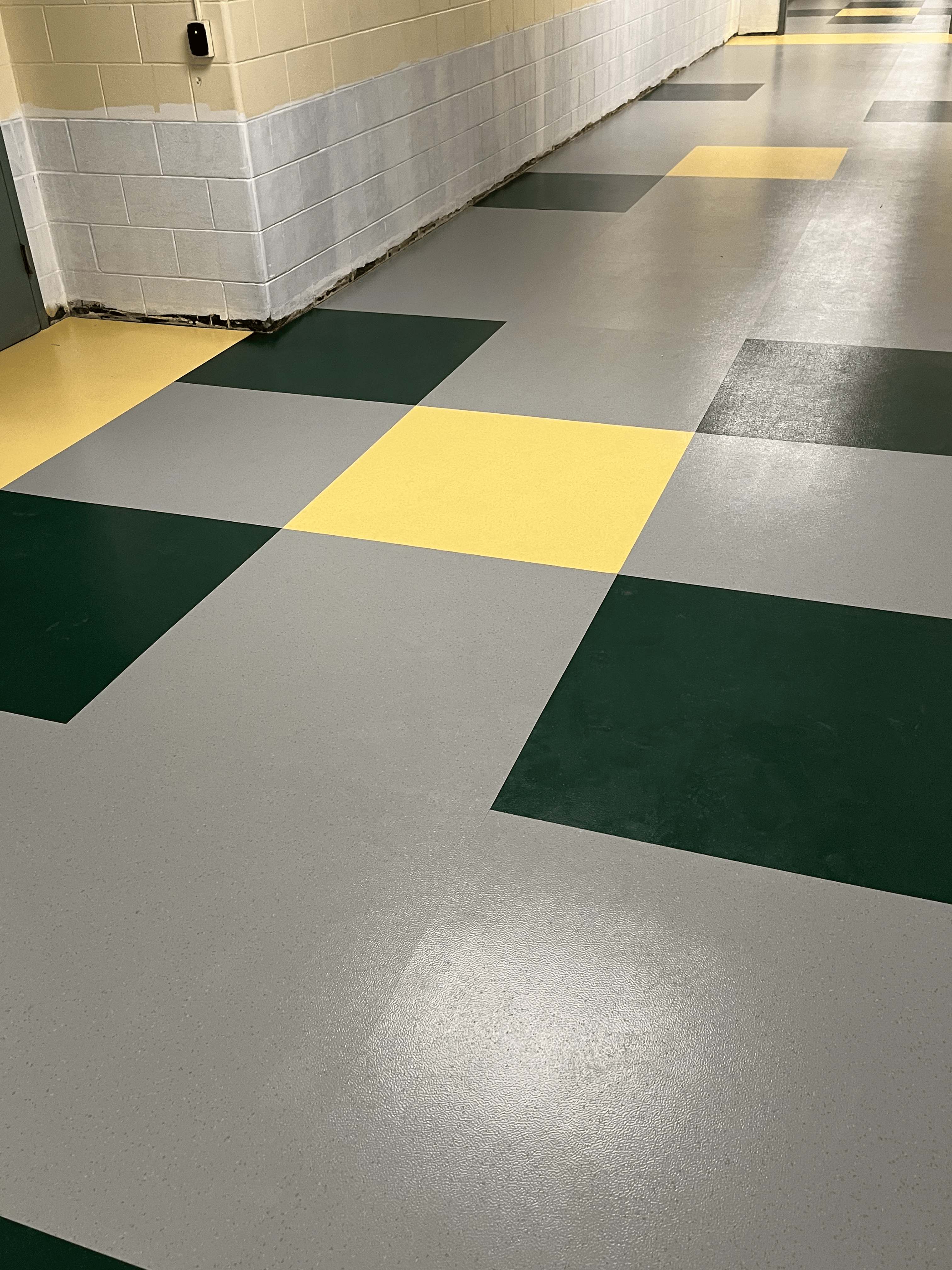 Green, gray, and yellow VCT tile floor in a school hallway