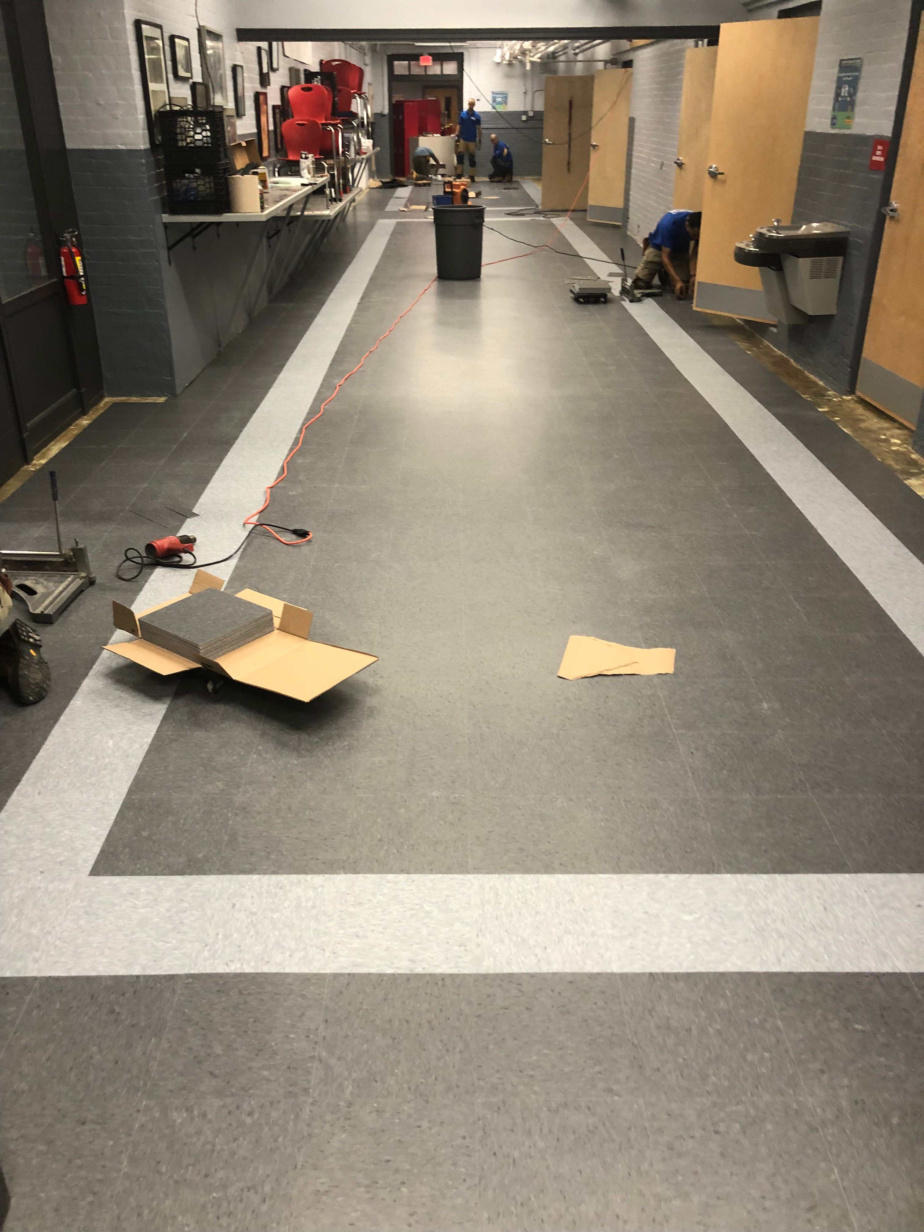 Installers laying gray VCT tile with white borders in a school hallway