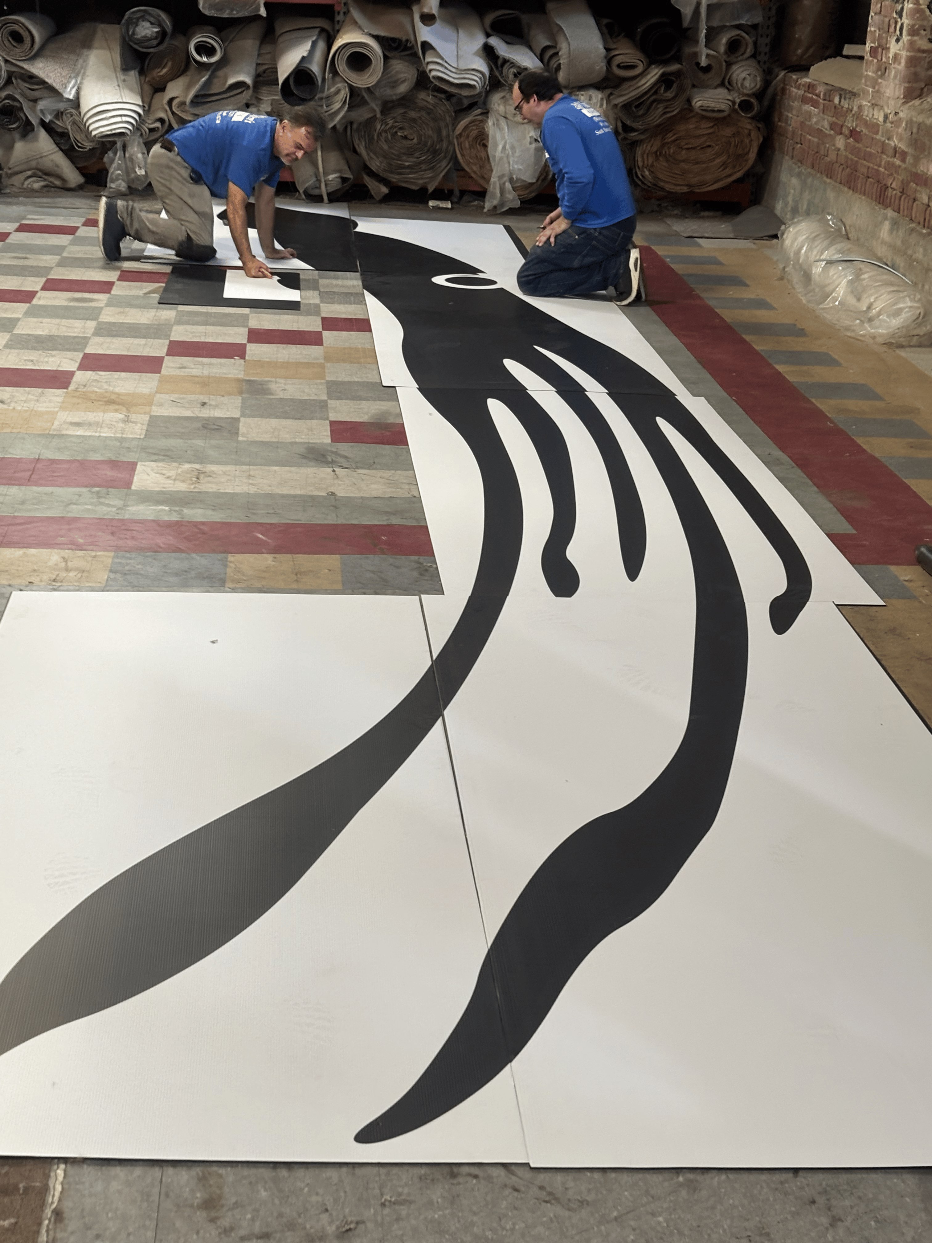 Two installers hand-cutting a large custom whale inlay in the workshop